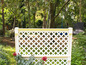 Bílý dřevěný mřížový plot s diamantovým vzorem v zelené zahradě.