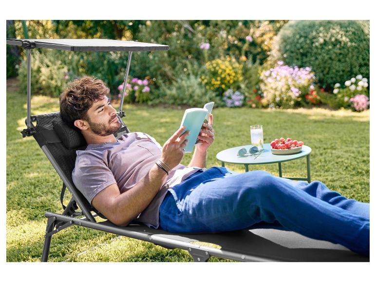 Muž relaxuje na zahradním lehátku se stínítkem, čte knihu na zahradě.