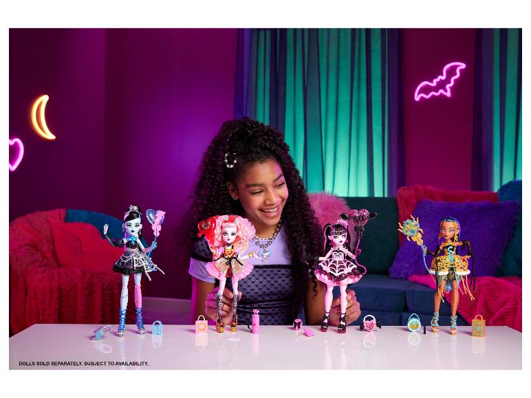 Usmívající se dívka drží panenky Monster High, s dalšími panenkami a doplňky na stole.