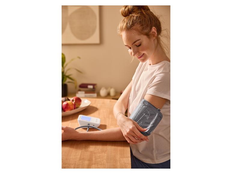 Žena si doma měří krevní tlak tlakoměrem.