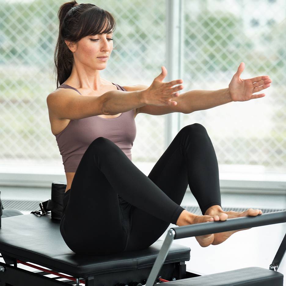 Žena cvičící Pilates na reformeru, v topu a černých legínách.