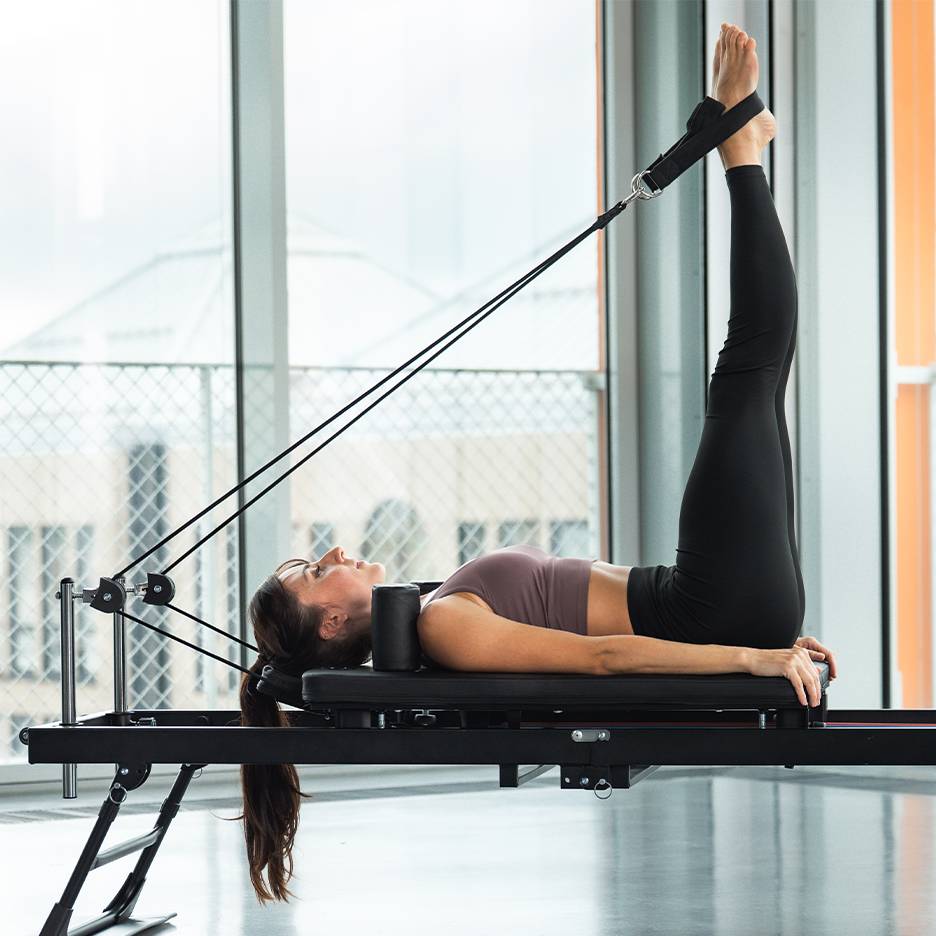 Žena cvičící nohy na pilates reformer stroji.