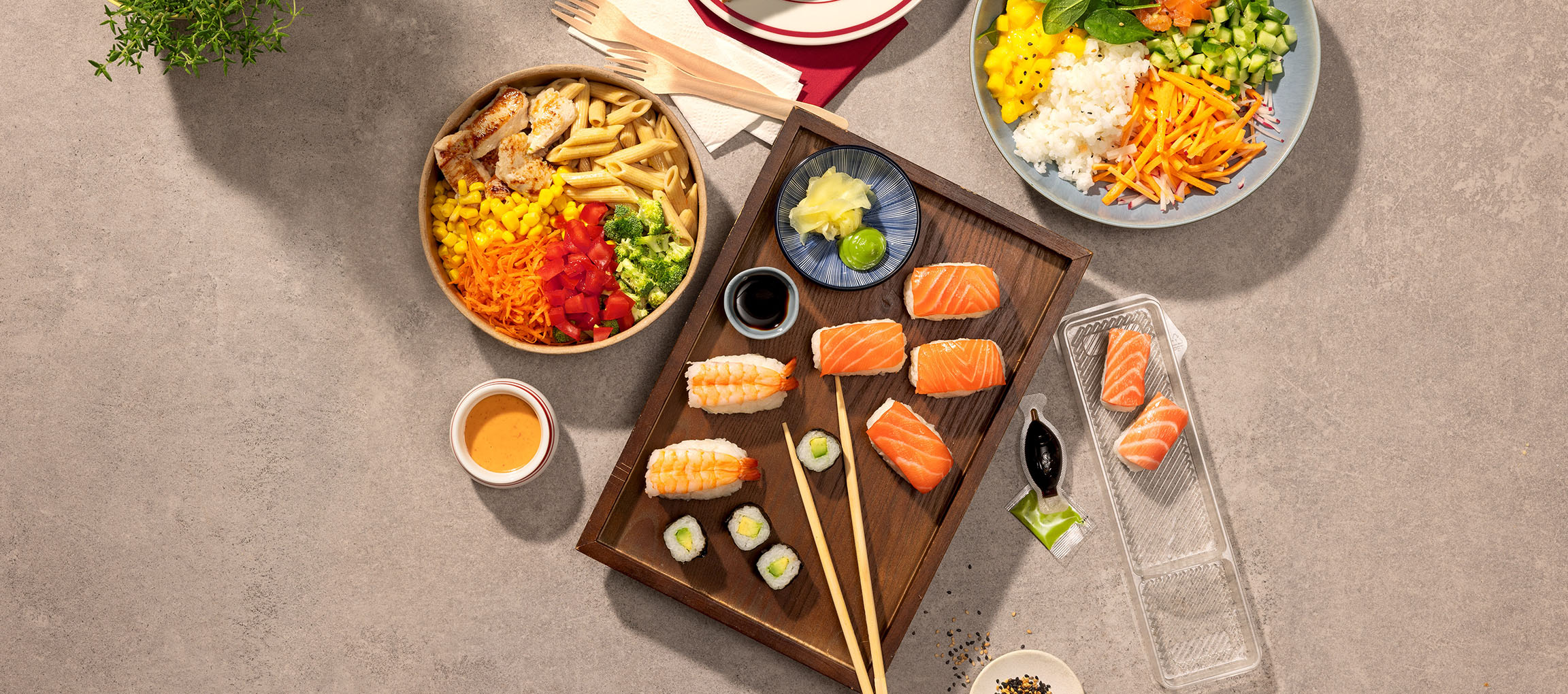 Různá jídla: miska s těstovinami a kuřecím masem, sushi a poke miska na stole.