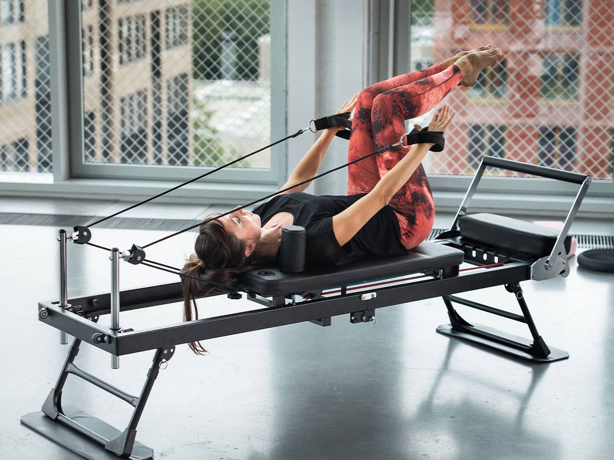 Žena cvičící Pilates na reformeru v červených legínách na jógu.