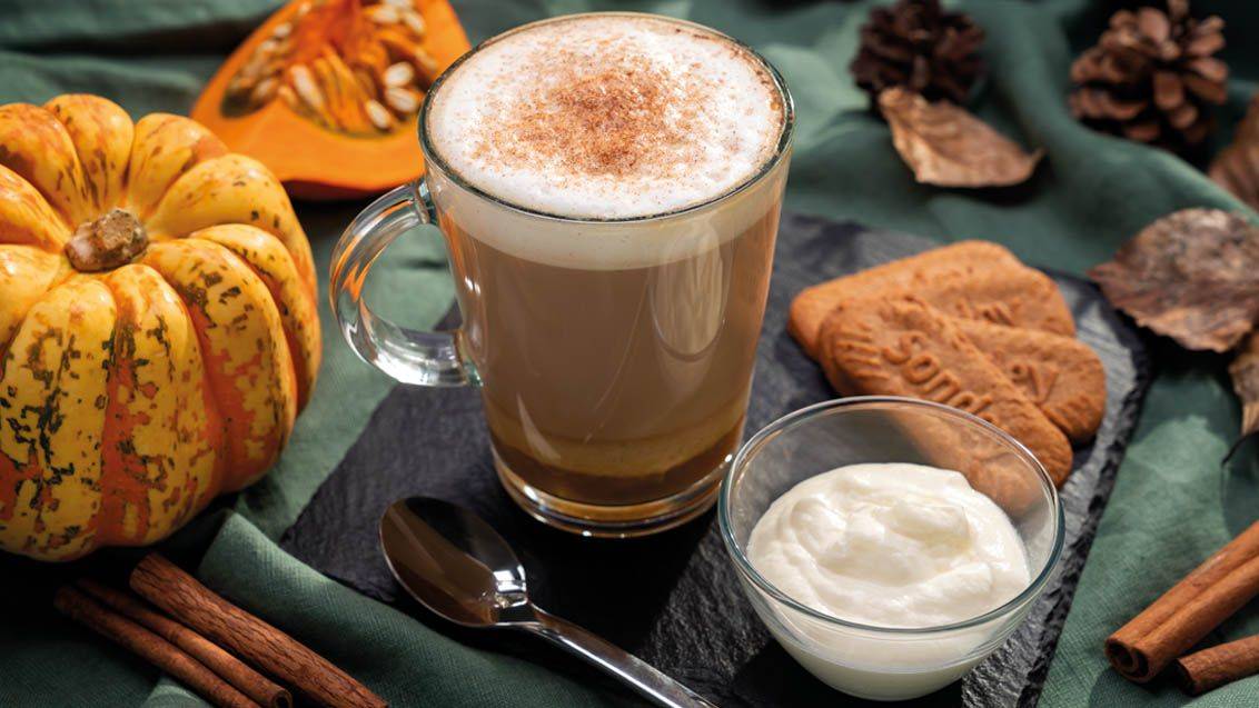 Dýňové latté s kořením, sušenkami a šlehačkou na podzimním pozadí.