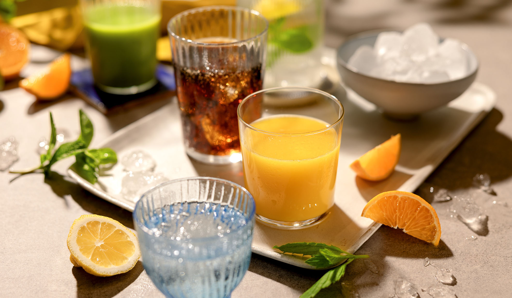 Různé osvěžující nápoje s ledem, plátky citrusů a mátou na tácu.