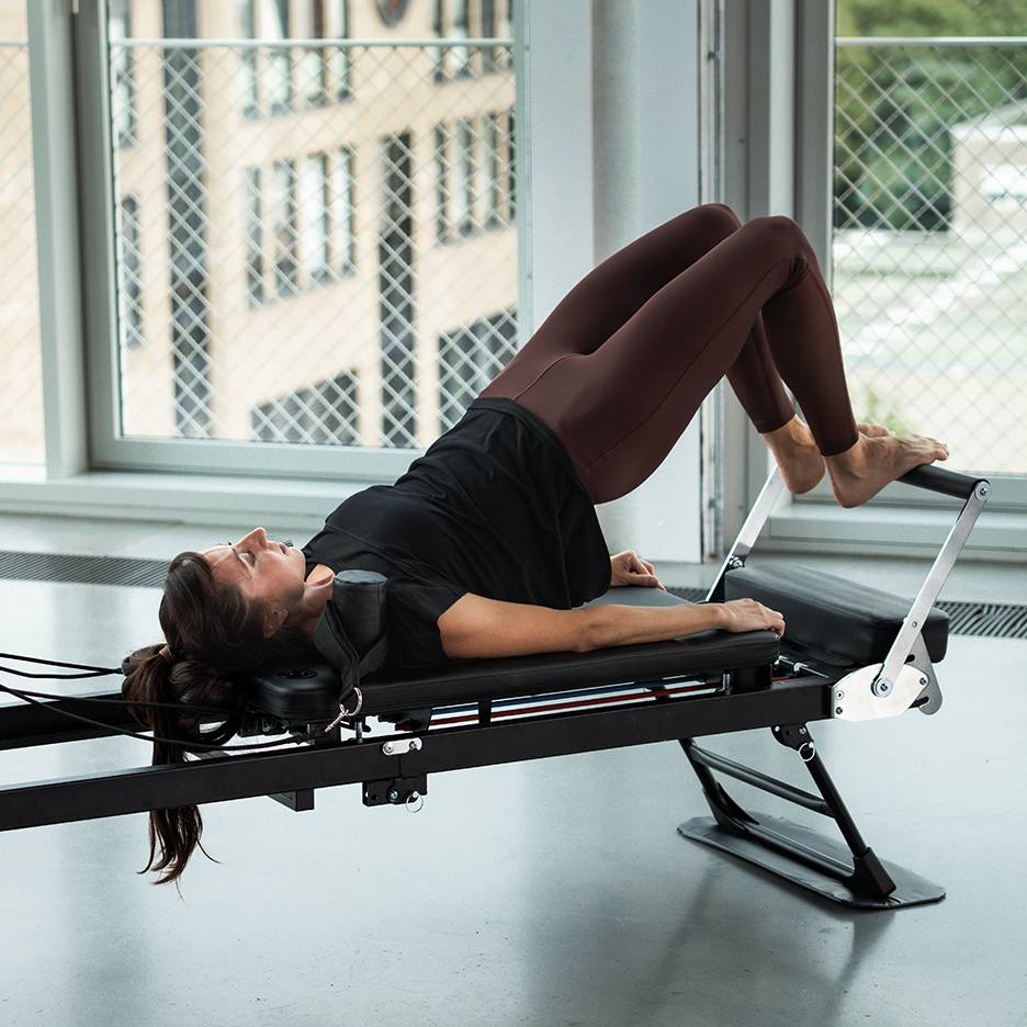 Žena cvičí Pilates na reformer stroji, nohy nahoře.