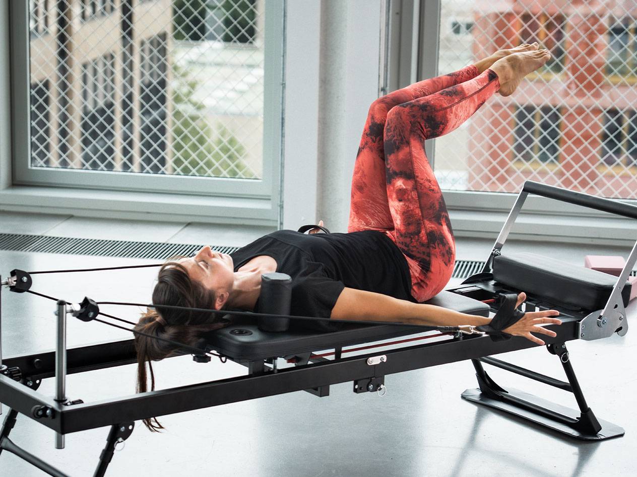 Žena cvičící Pilates na reformeru, v červeno-černých legínách