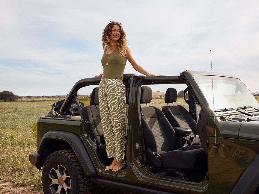 Žena stojící na jeepu v khaki tílku a bílo khaki kalhotách