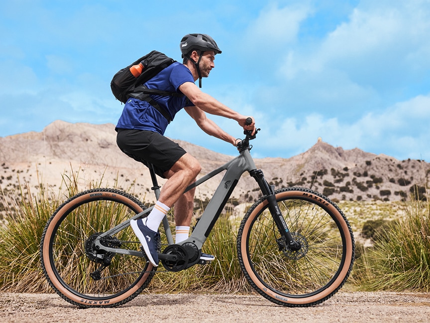 Cyklista na kole jede po štěrkové cestě v kopcovité krajině.