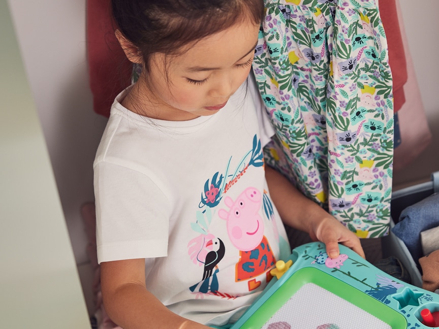 Dívka v tričku Peppa Pig si kreslí na dětskou kreslicí tabulku.