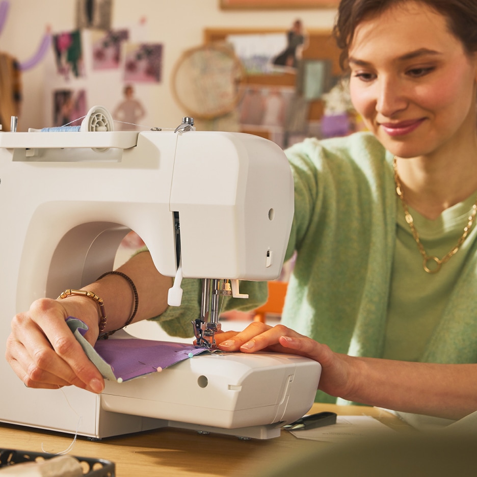 Žena šije na šicím stroji fialovou látku.