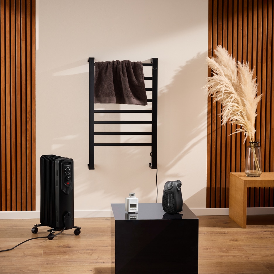 Koupelna s černým sušákem na ručníky, olejovým radiátorem a malým topením.