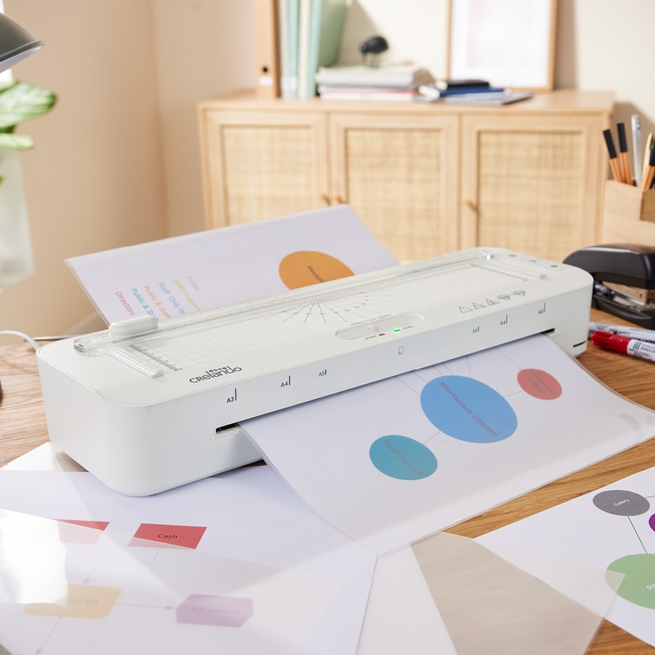 Bílý laminátor CRELANDO laminuje dokumenty s grafy na dřevěném stole.