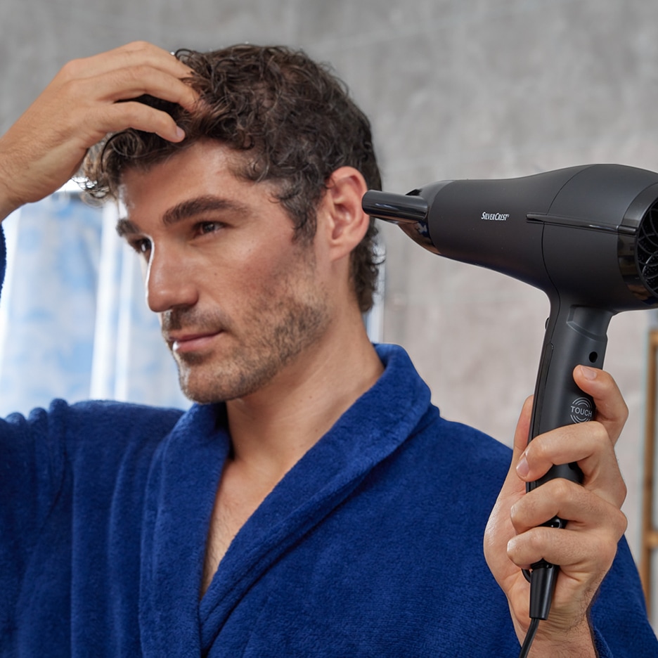 Muž v županu si suší vlasy fénem SilverCrest.