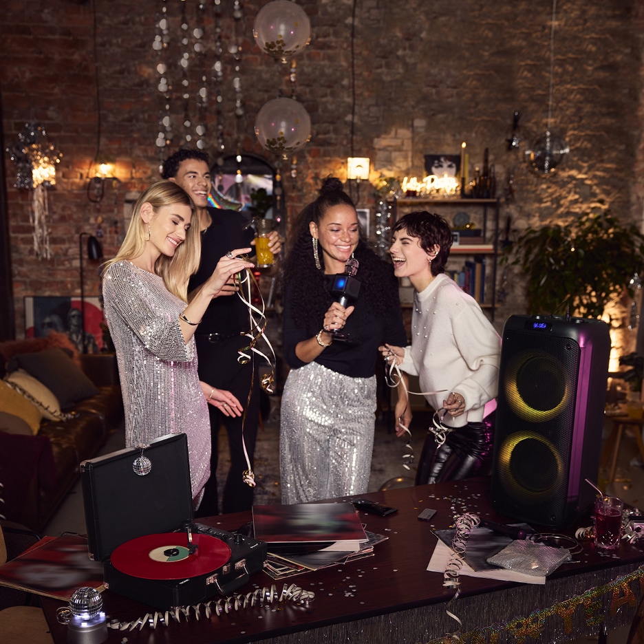 Přátelé se baví na večírku s karaoke mikrofonem, gramofonem a párty reproduktorem.