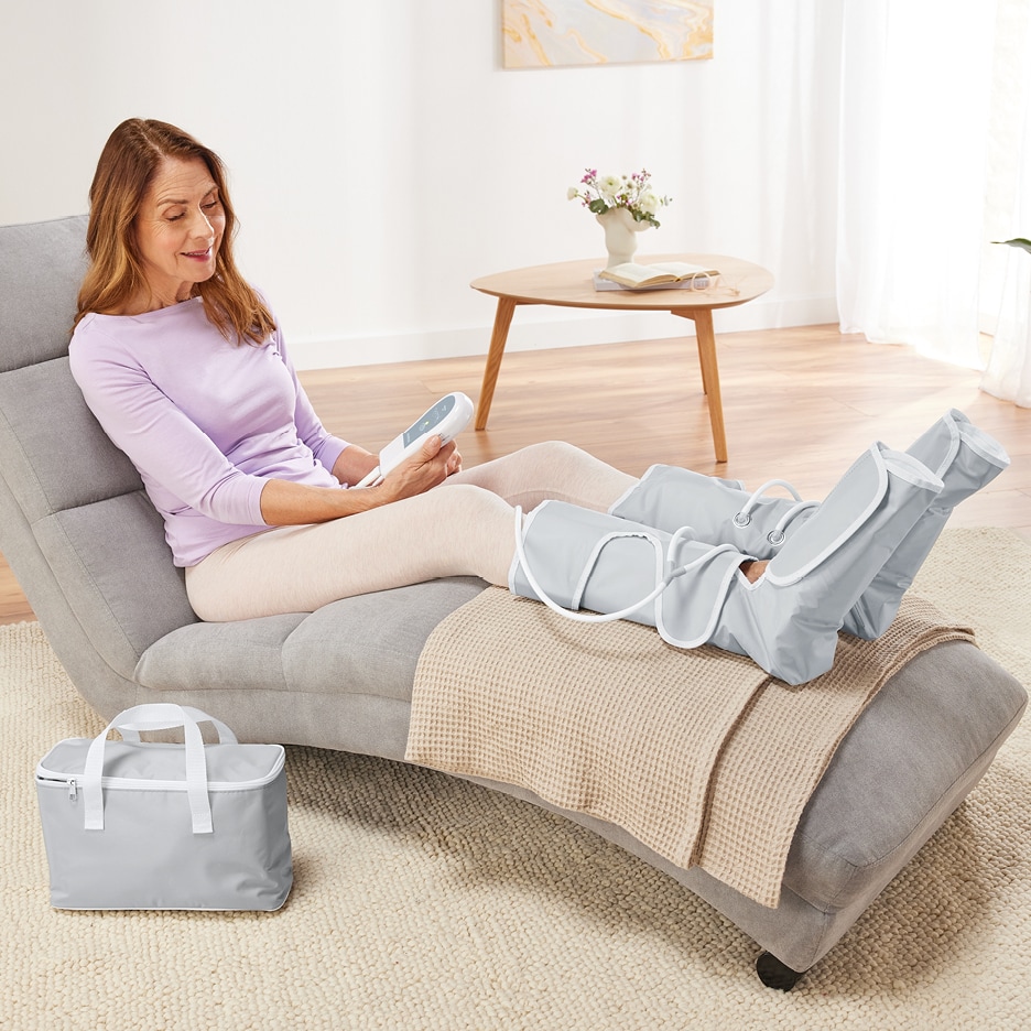 Žena relaxuje na lehátku s masážními návleky na nohy a ovladačem v ruce.