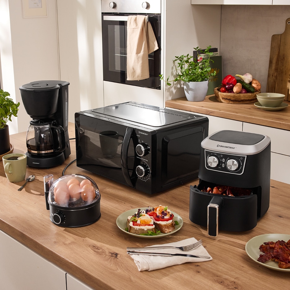 Kuchyňská linka s černými spotřebiči SilverCrest: mikrovlnná trouba, kávovar, horkovzdušná fritéza a vařič vajec.