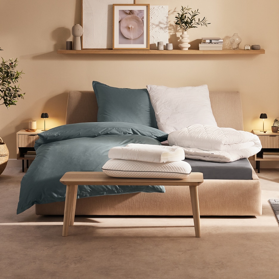 Ložnice s postelí, modrým povlečením a bílými polštáři a přikrývkami.