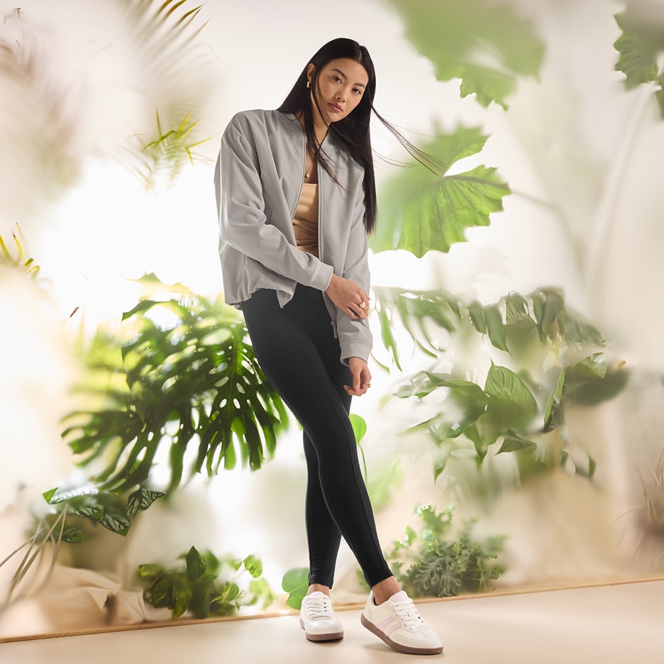 Žena v šedé bundě, černých legínách a bílých teniskách s růžovými pruhy