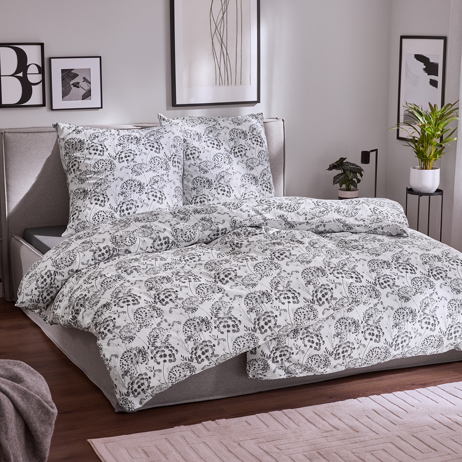 Bílé povlečení s černým květinovým vzorem na posteli v ložnici.