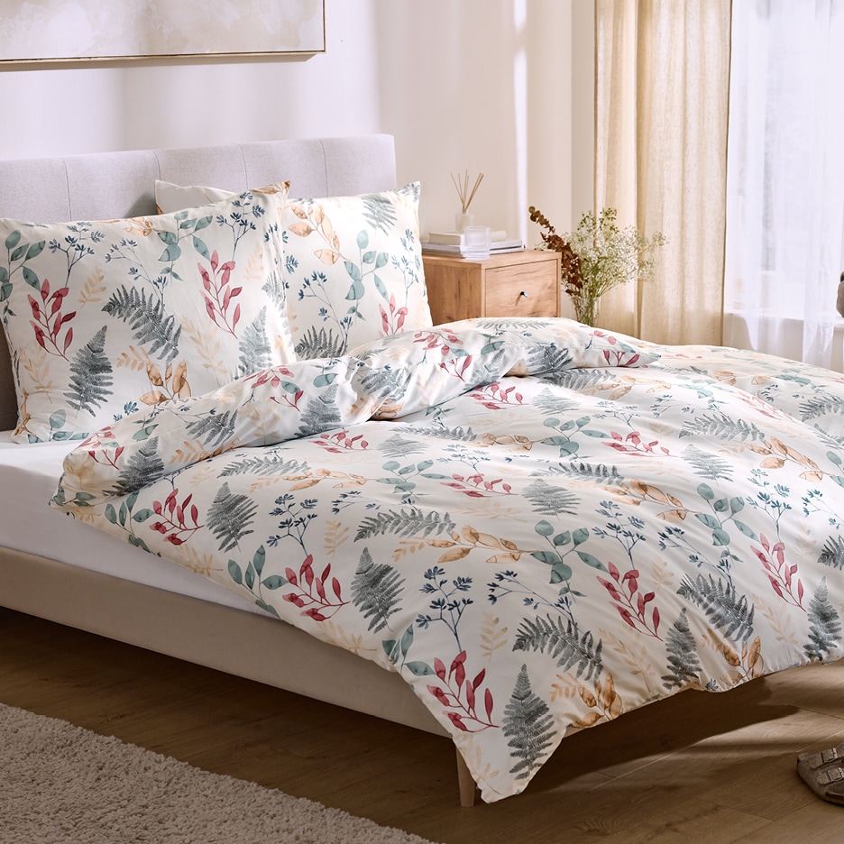 Bílé povlečení s botanickým vzorem listí v ložnici s dřevěným nočním stolkem.