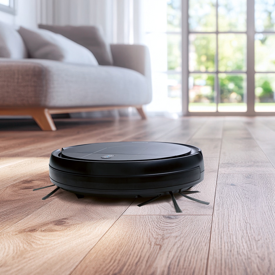 Černý robotický vysavač na dřevěné podlaze v obývacím pokoji.