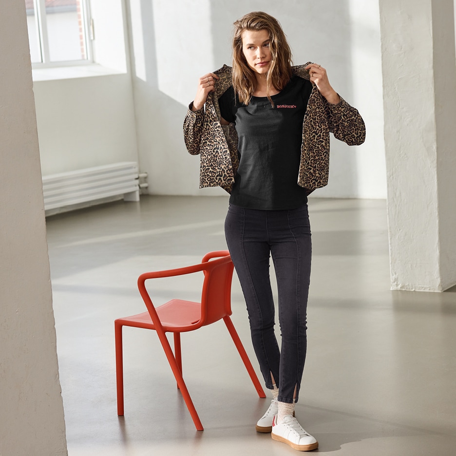 Žena v leopardí bundě, černém tričku s nápisem „BONJOUR“ a tmavých džínách s rozparky.