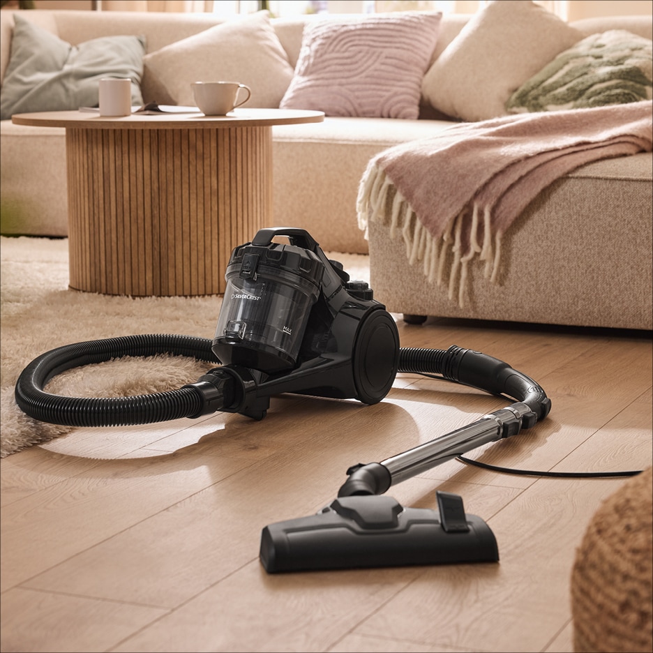 Černý vysavač s hadicí a hubicí na dřevěné podlaze v obývacím pokoji.