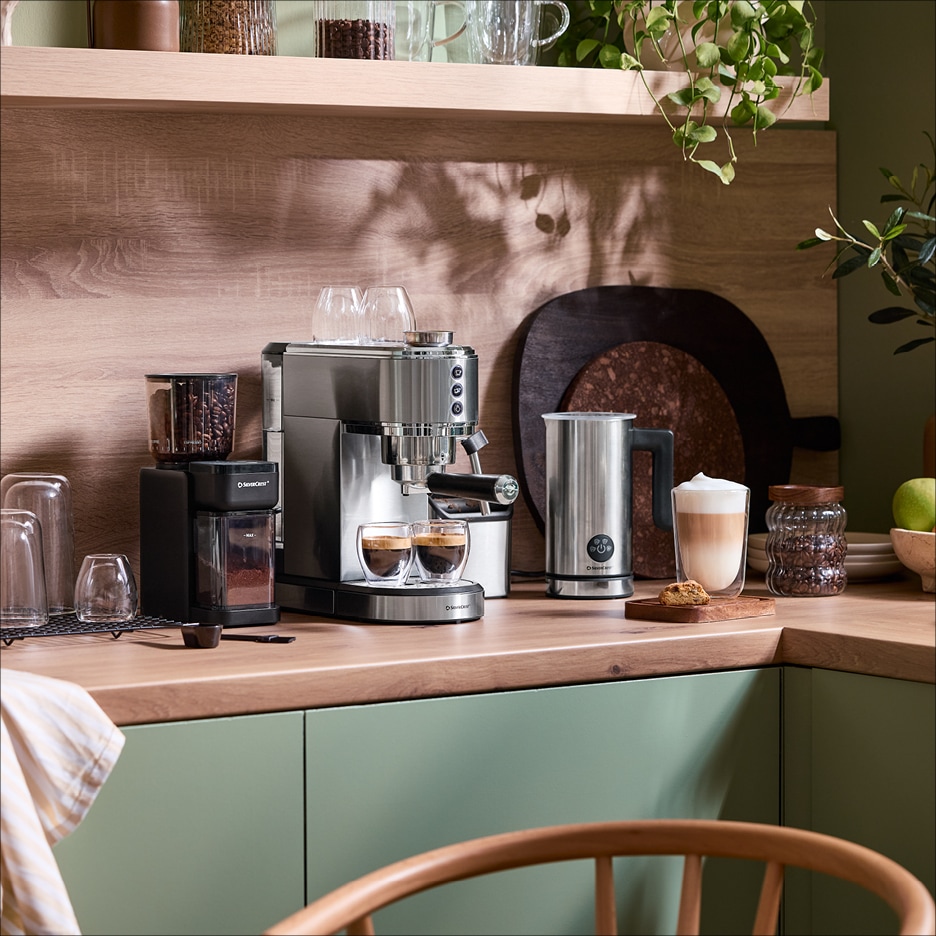 Espresso kávovar a mlýnek na kávu na dřevěné kuchyňské lince se zelenými skříňkami.