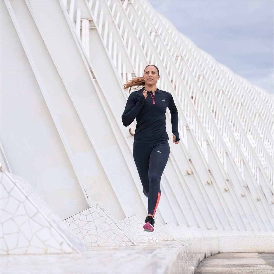 Žena v tmavě modrém sportovním oblečení běží venku.