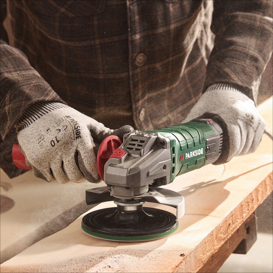 Muž v rukavicích brousí dřevěné prkno úhlovou bruskou.