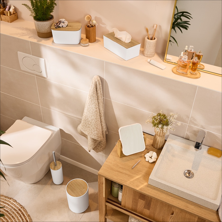 Koupelna s toaletou, umyvadlem a dřevěnými doplňky, včetně dávkovače kapesníků a úložných boxů.