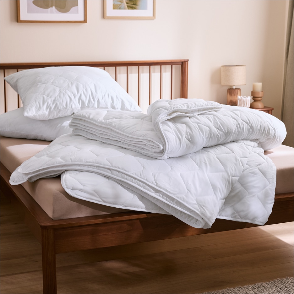 Bílé prošívané přikrývky a polštáře na dřevěné posteli v ložnici.