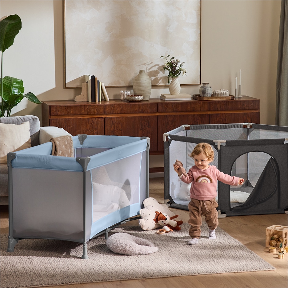 Dětská cestovní postýlka a ohrádka v obývacím pokoji s batoletem.