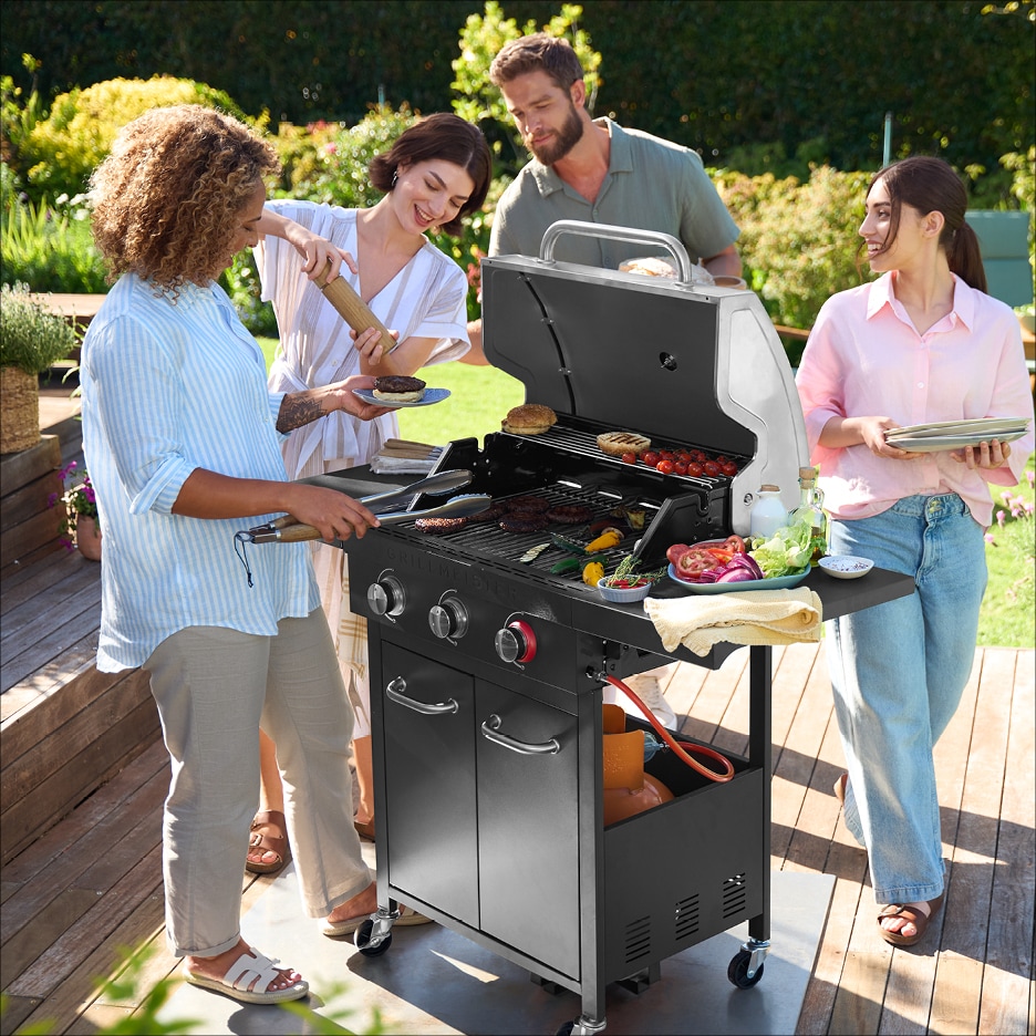 Lidé grilují na zahradě, připravují jídlo na plynovém grilu.