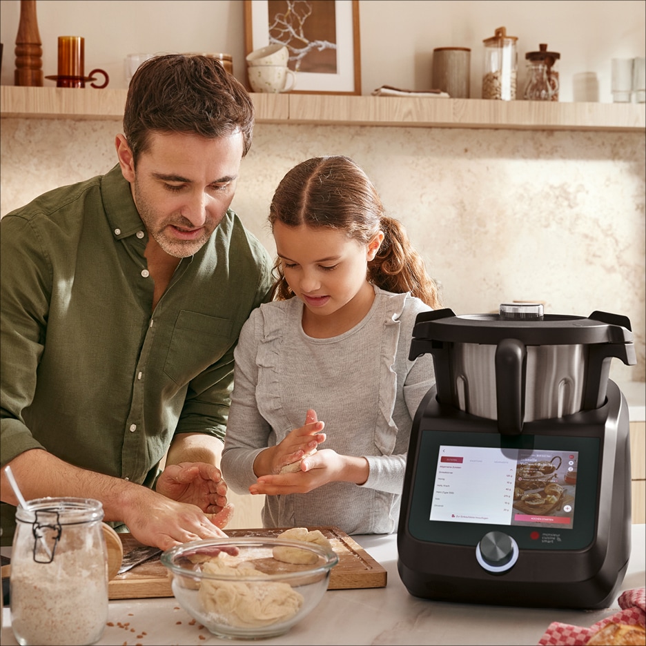 Otec a dcera připravují těsto v kuchyni s chytrým kuchyňským robotem.
