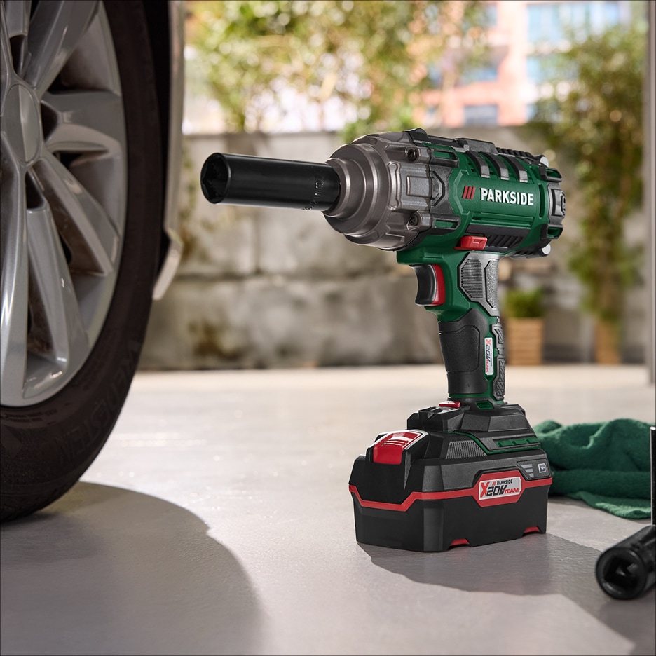 Akumulátorový rázový utahovák s baterií a nástavcem na kola u auta.