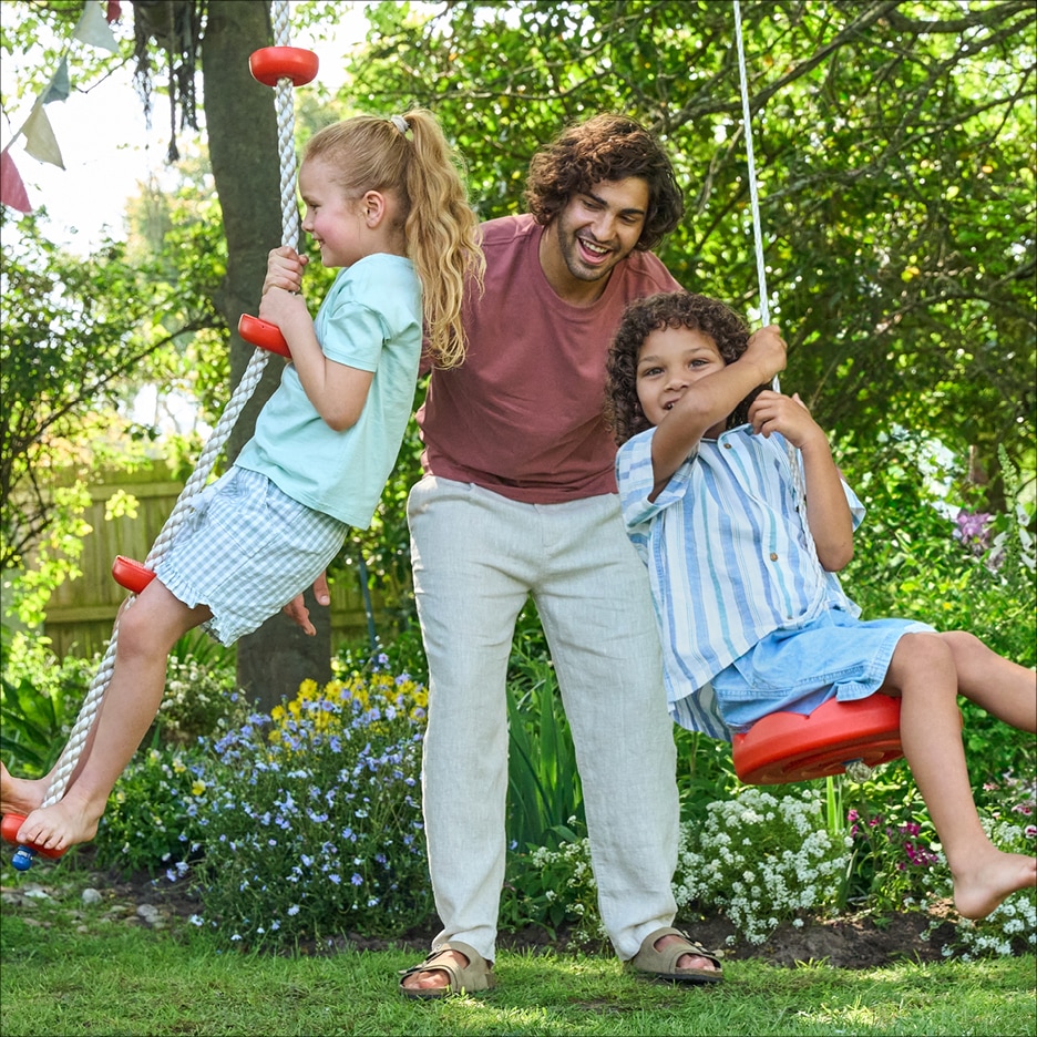Muž a dvě děti si hrají na houpačkách v zahradě.