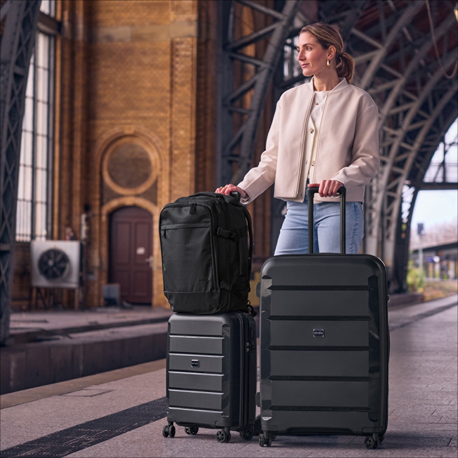 Žena s černými kufry a batohem na nádraží.