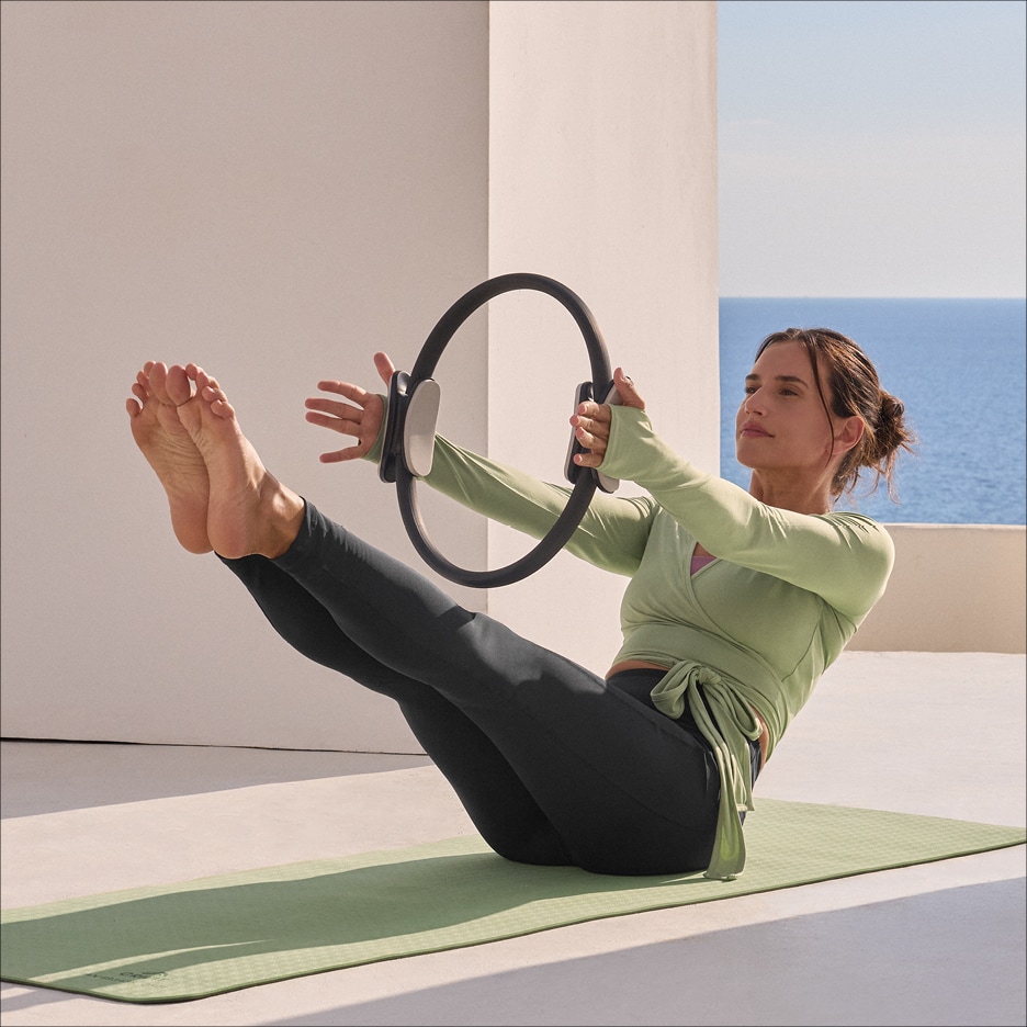 Žena cvičící pilates s kruhem na podložce, oblečená v legínách a topu.