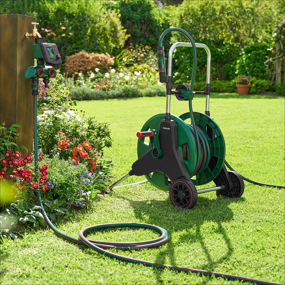 Zahradní hadice na vozíku a časovač zavlažování u vodovodního kohoutku v zahradě.
