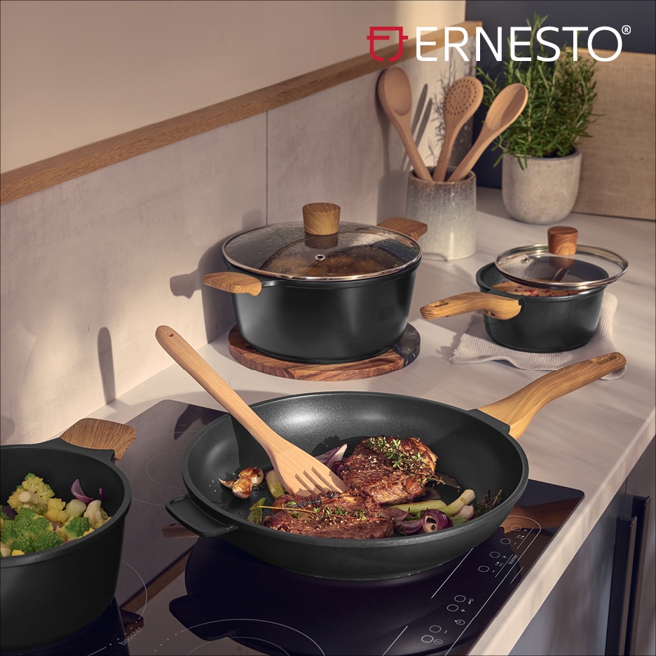 Sada černého nádobí s dřevěnými rukojeťmi a pokličkami, s masem a zeleninou na sporáku.