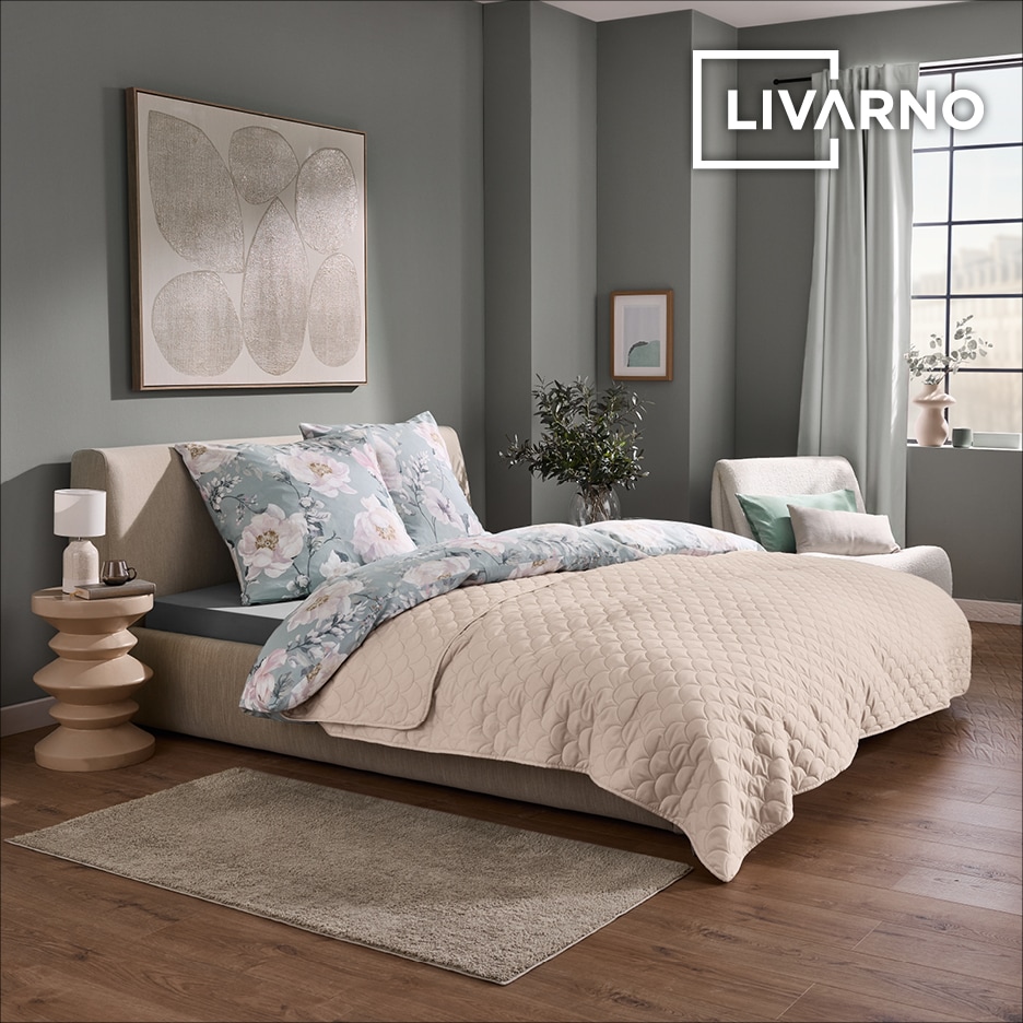 Ložnice s béžovou prošívanou dekou, květinovým povlečením a moderním uměním na stěně.