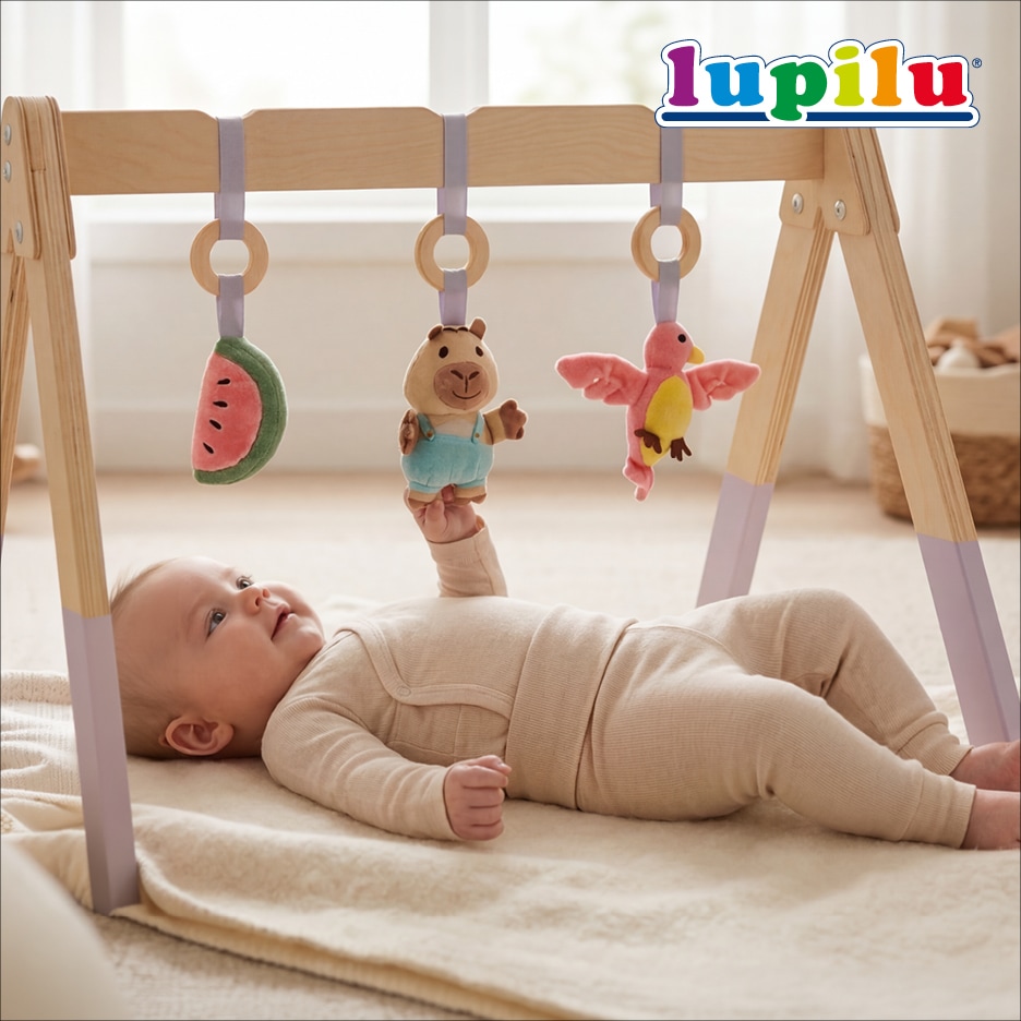 Dítě ležící na dece si hraje s dřevěnou hrazdičkou s plyšovými hračkami.