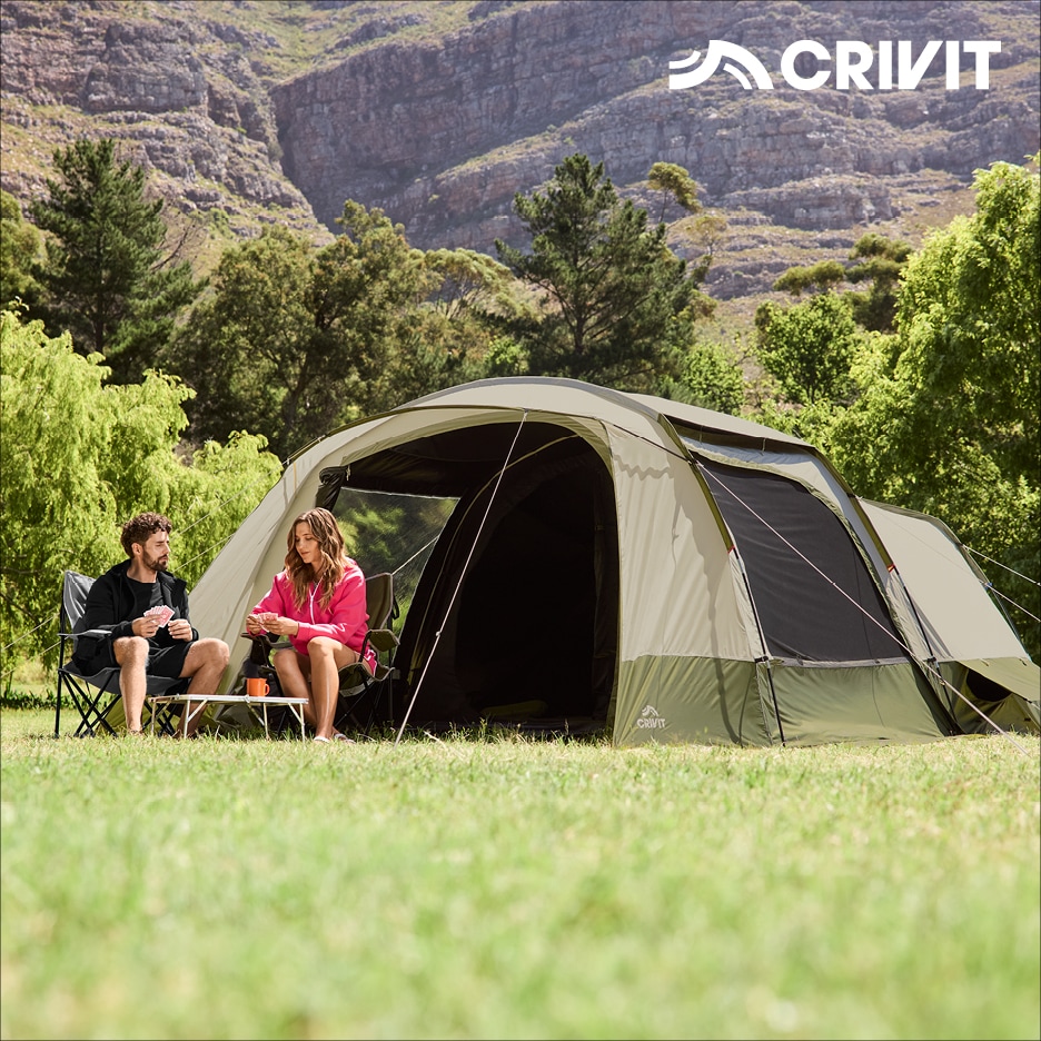 Pár kempuje s velkým stanem a skládacími židlemi v horách.