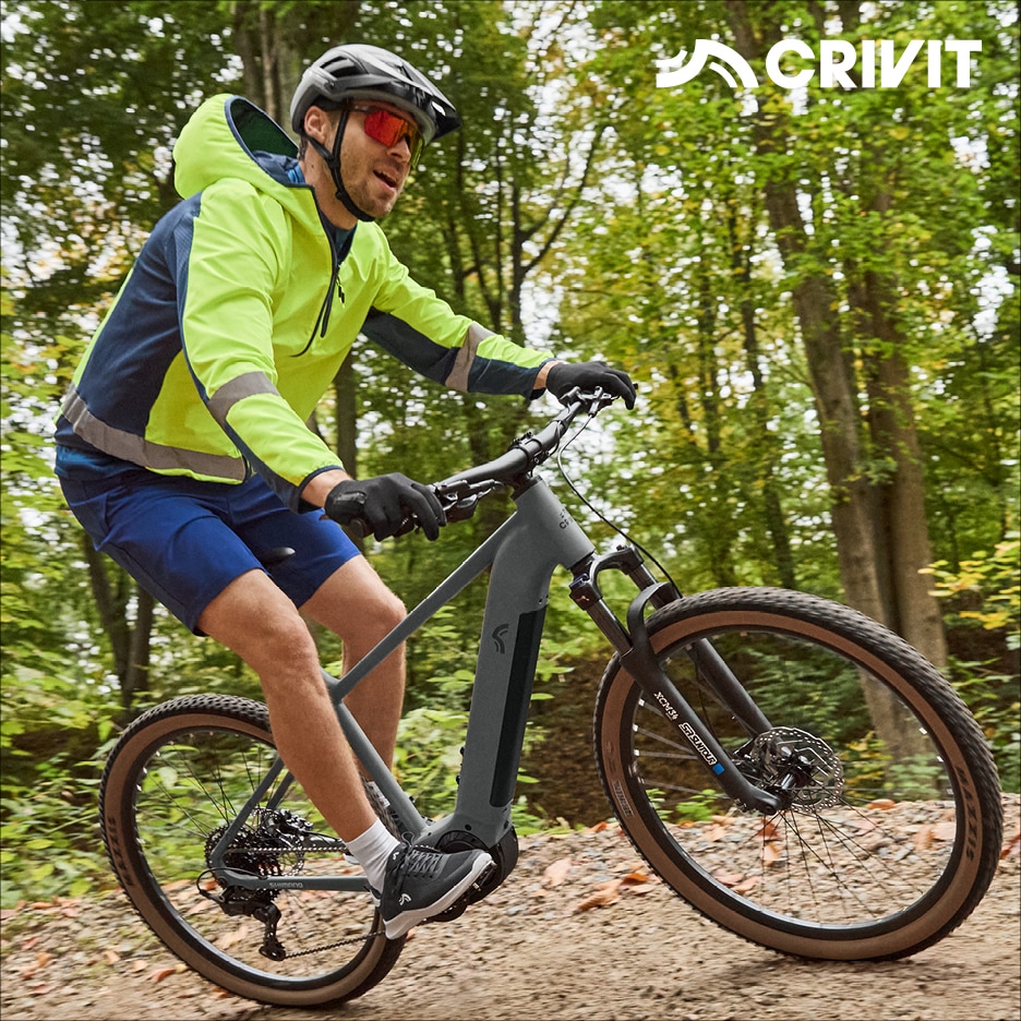 Muž na horském elektrokole v reflexní bundě a šortkách v lese.