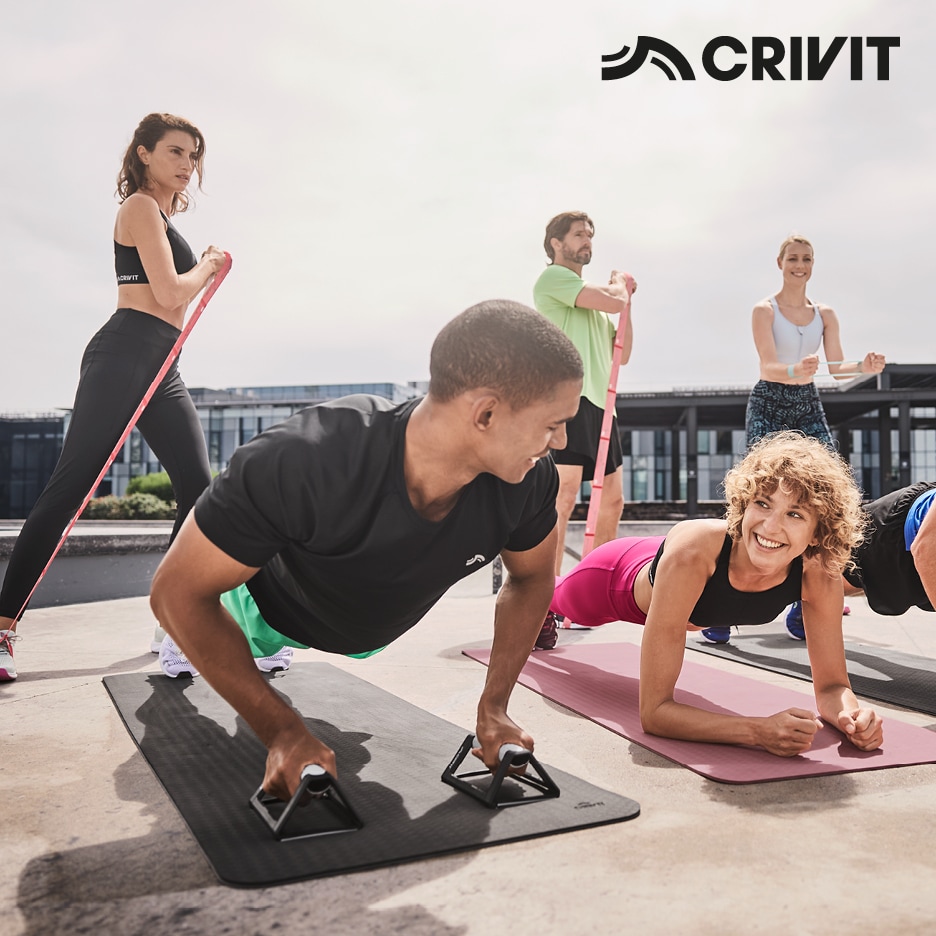 Skupina lidí cvičících venku s fitness vybavením, jako jsou podložky, posilovací gumy a madla na kliky.