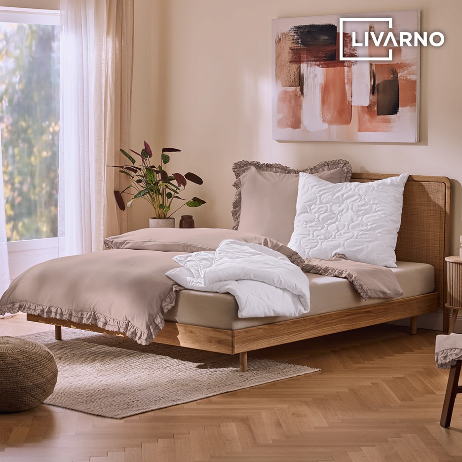 Ložnice s dřevěnou postelí, béžovým povlečením s volánky a bílou přikrývkou.