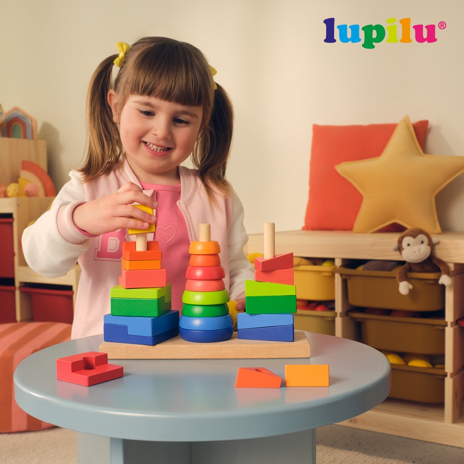 Dívka si hraje s dřevěnými skládacími hračkami na stole.